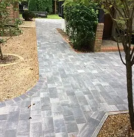 Block paved path curving through a gravel front garden