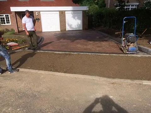 Red block paved driveway being finished with a plate compactor outside a garage
