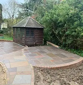 Curved sandstone patio with a brick edge in front of a timber summerhouse