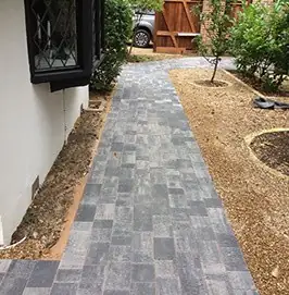 Grey block paved path running along a house to a side gate