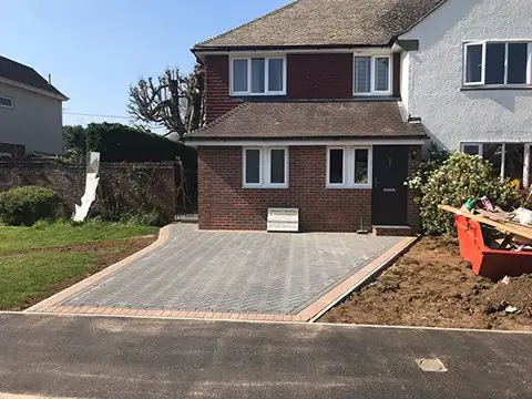 Grey herringbone block driveway with a buff border in front of a newly built semi-detached house