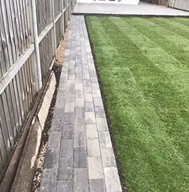 New lawn edged by a block paved path and a timber fence