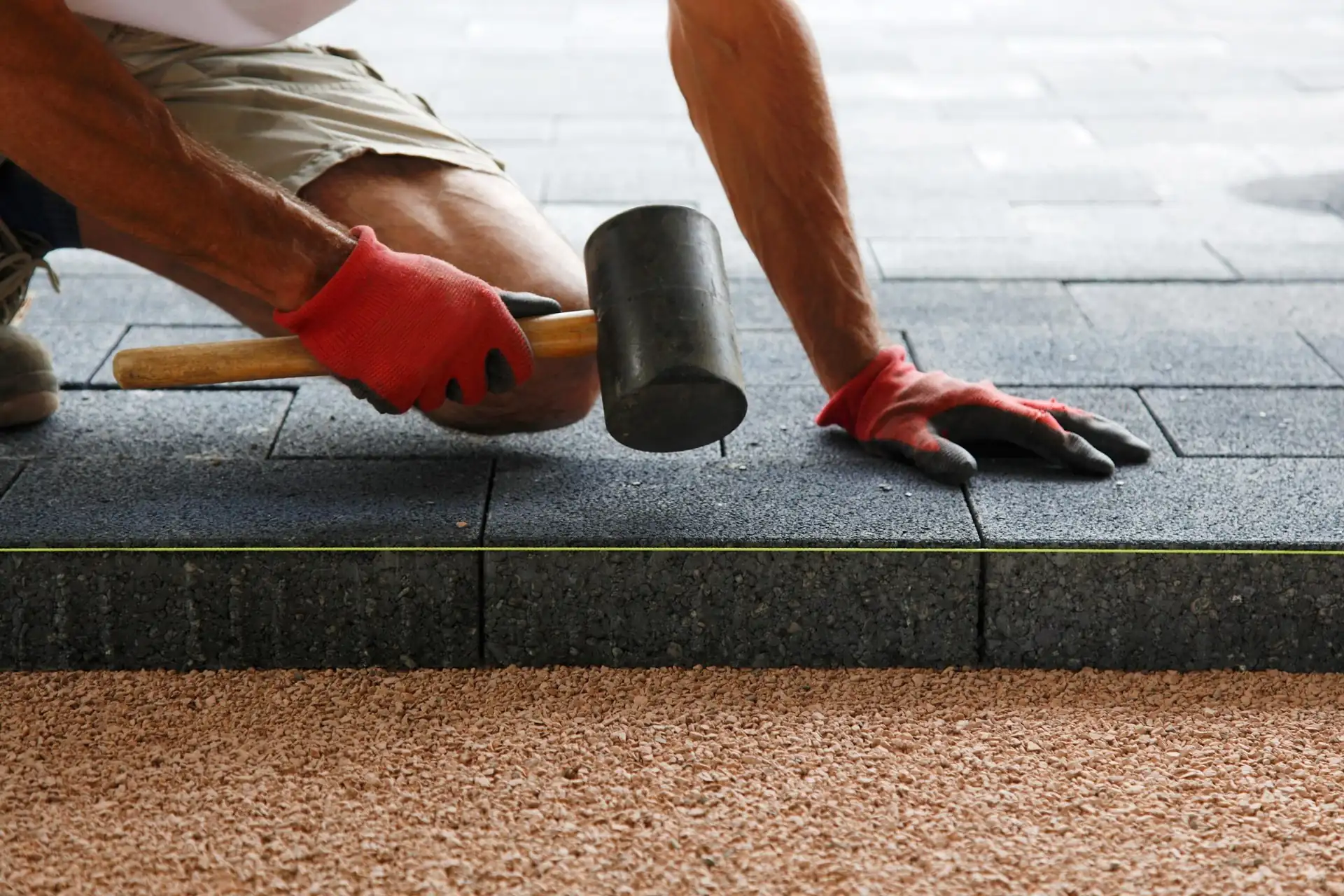 Paver setting a grey paving slab into place with a rubber mallet