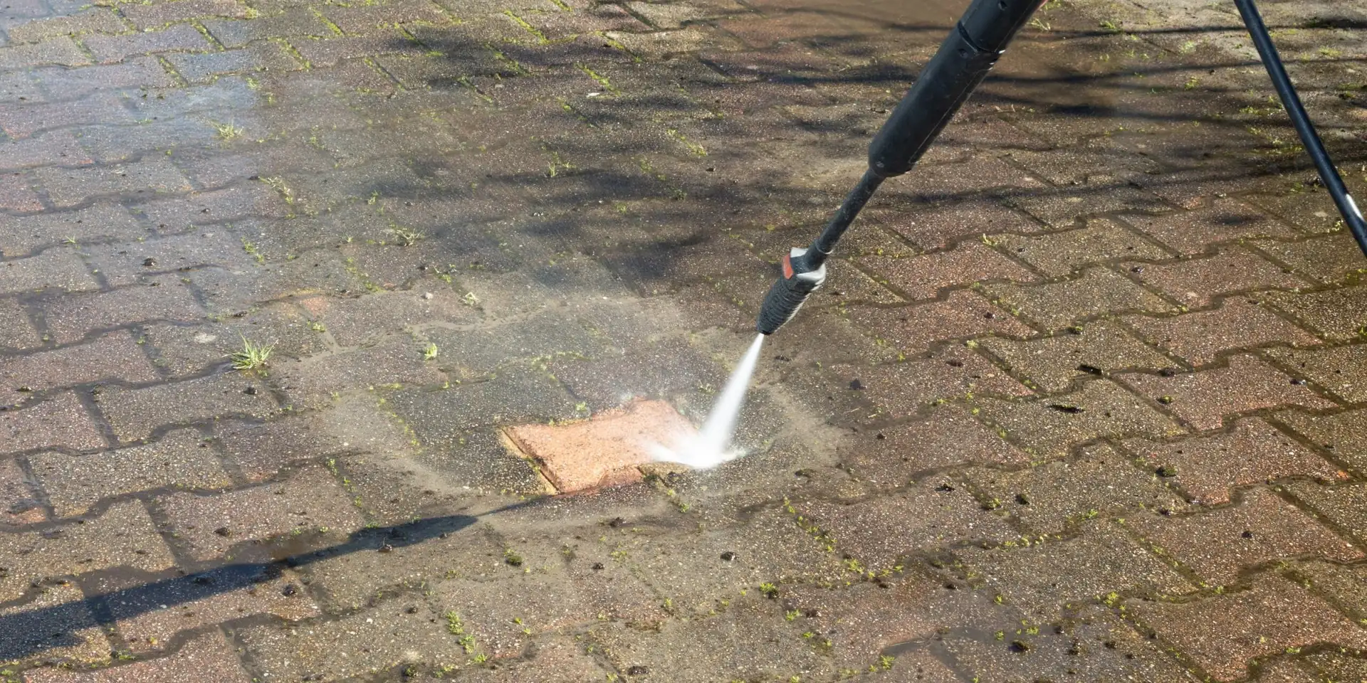 Pressure washer cleaning a strip of weathered block paving