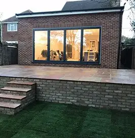 Raised sandstone patio with a brick retaining wall and steps down to a new lawn