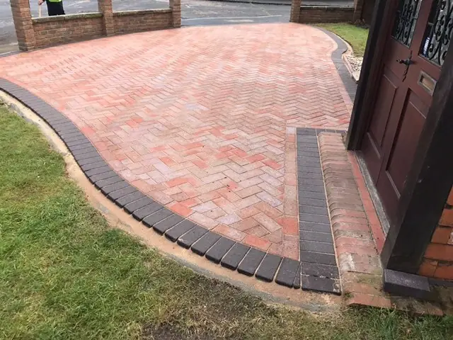 Red clay herringbone paving curving to a front door with a charcoal edge