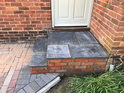 Grey slab step with red brick risers leading up to a front door