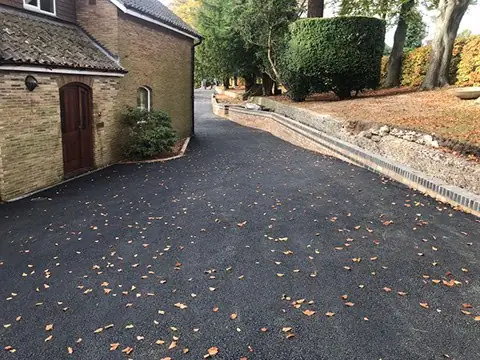 New tarmac driveway following the slope alongside a detached house with brick edging