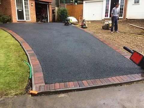 New tarmac driveway edged with red blocks outside a detached house
