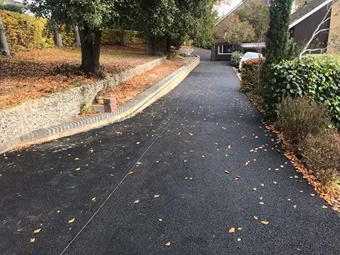 Tarmac driveway sweeping up a tree-lined slope with block edging