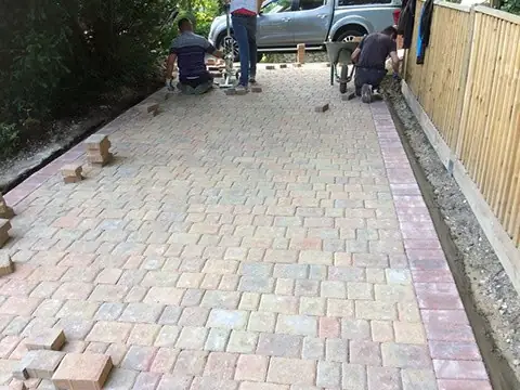 Team laying tumbled block paving on a new driveway beside a timber fence in Godalming