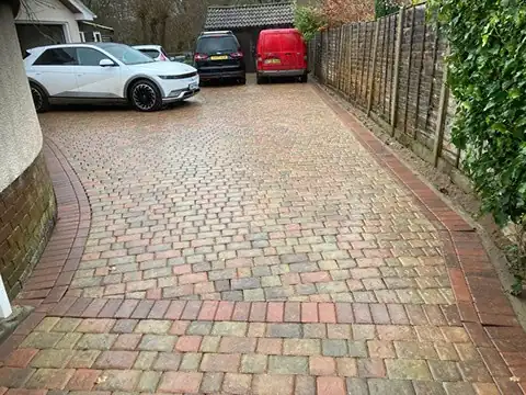 Tumbled cobble-effect block paved driveway with cars parked beside a house